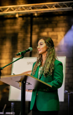 Person in a green blazer speaking at a podium with a microphone. Person in a green blazer speaking at a podium with a microphone.