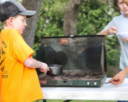 Child in a yellow shirt using a camp stove outdoors. Child in a yellow shirt using a camp stove outdoors.