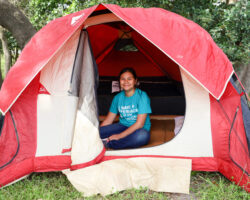 Person sitting inside a red and white camping tent. Person sitting inside a red and white camping tent.