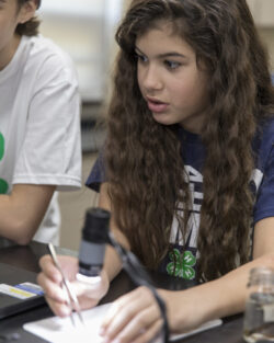 Exploring microscopic details in a STEM lab. Student using tweezers and a microscope for a science experiment in a classroom setting.