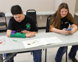 Hands-on electronics activity in STEM education. Two students working on an electronics project with wires and a circuit board at a classroom table.