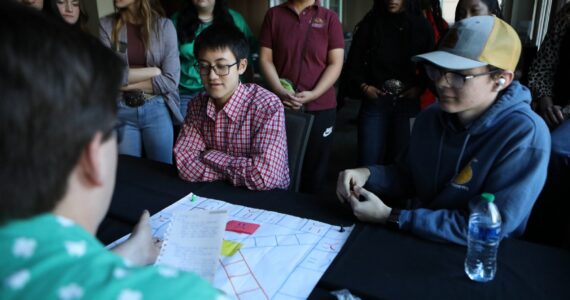 Group of students engaged in a business strategy board game during classroom activity.
