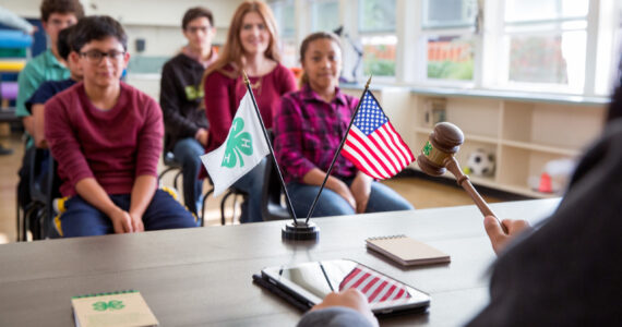 Texas 4-H club meeting with U.S. and 4-H flags, teaching leadership and parliamentary skills.