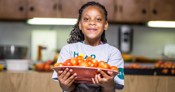 Person holding a bowl filled with fresh tomatoes in a kitchen setting.