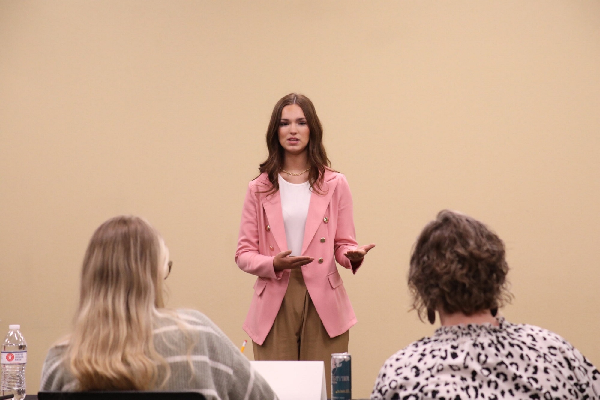 Presenting a prepared speech during a public speaking contest. Individual standing and delivering a presentation to two seated judges in a classroom setting.