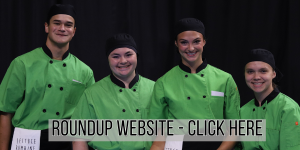 Four individuals wearing matching green chef jackets and black aprons stand together in front of a dark backdrop. A banner across the bottom of the image reads: “ROUNDUP WEBSITE – CLICK HERE.”